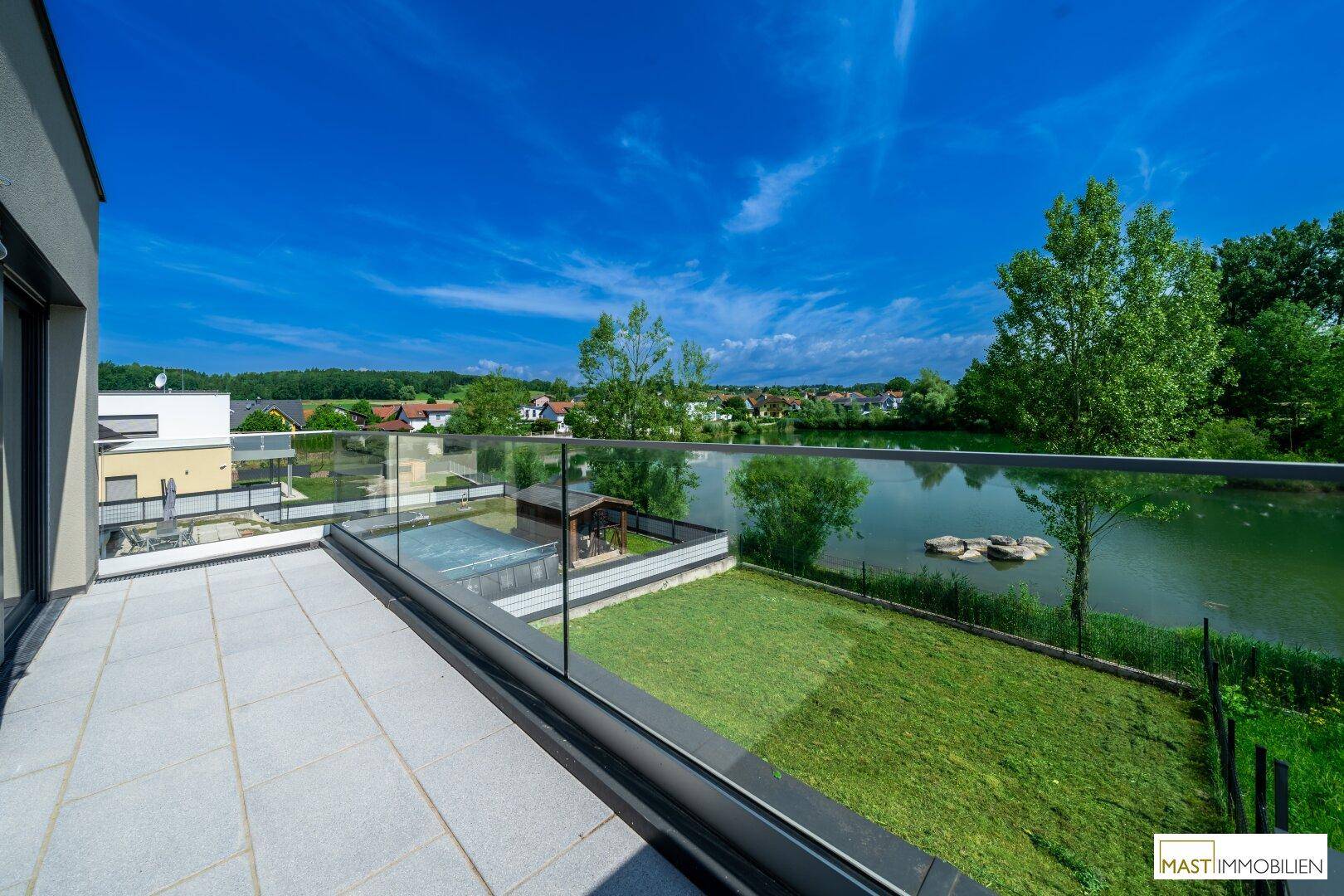 Großer Balkon mit Fliesenboden und Glasbrüstung, der einen Panoramablick auf den See und die Nachbarschaft bietet.