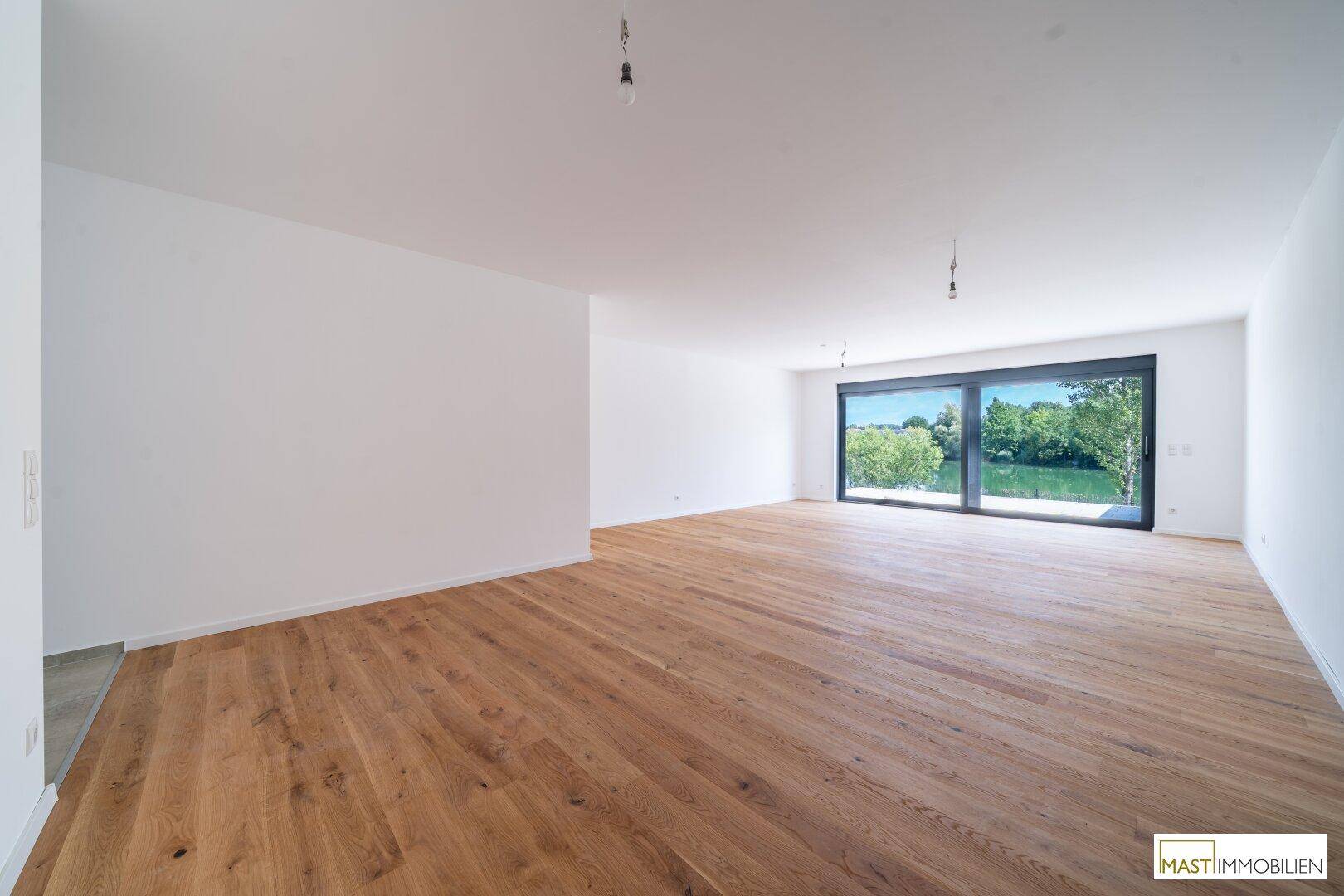 Großzügiges, leeres Wohnzimmer mit Eichenparkett und bodentiefen Fenstern mit Blick ins Grüne.