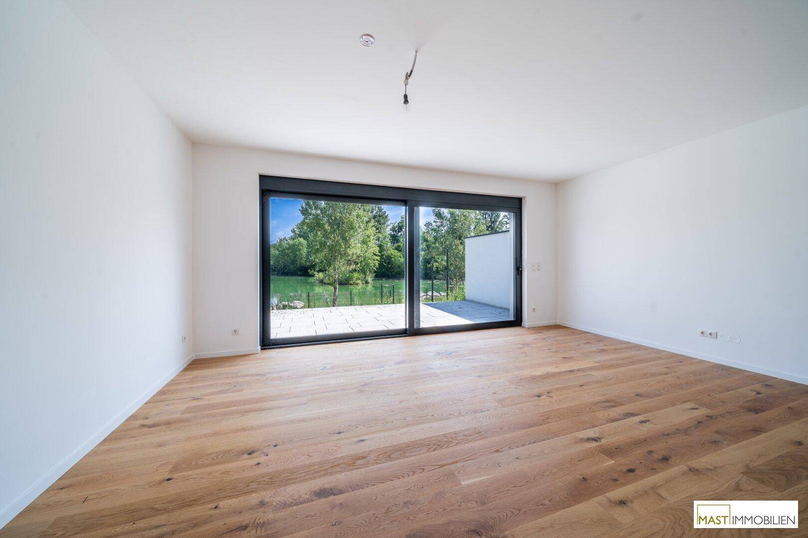 Helles Wohnzimmer mit Holzboden und großer Schiebetür, die einen direkten Blick auf den See bietet.