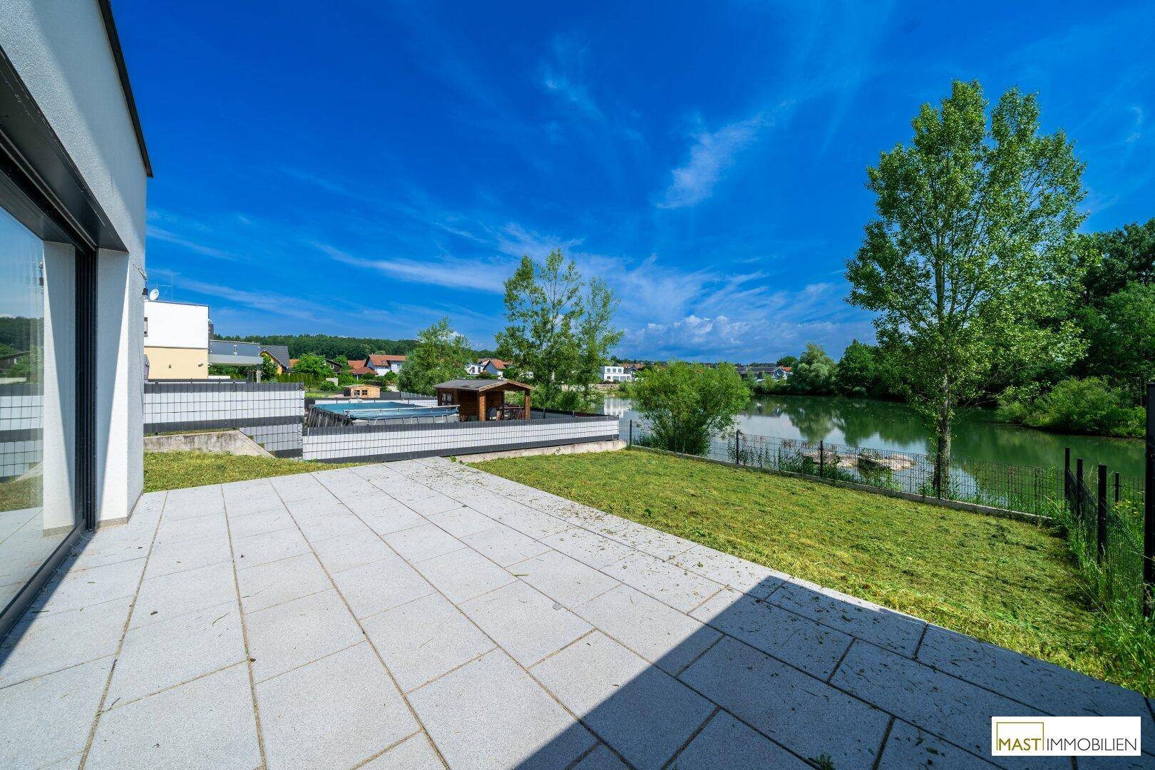 Große Terrasse mit Fliesenboden und direktem Zugang zum Garten, mit Blick auf den See und einen kleinen Pool.