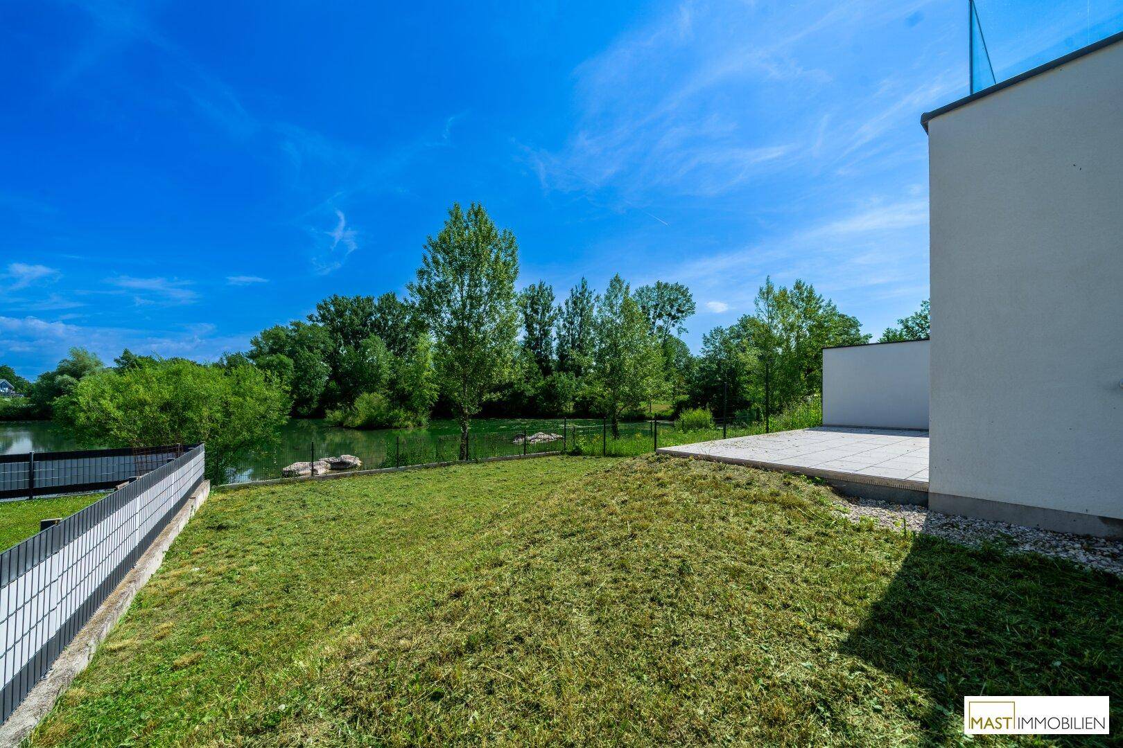 Gepflegter Gartenbereich mit Rasenfläche und direktem Zugang zum See, umgeben von grünen Bäumen.