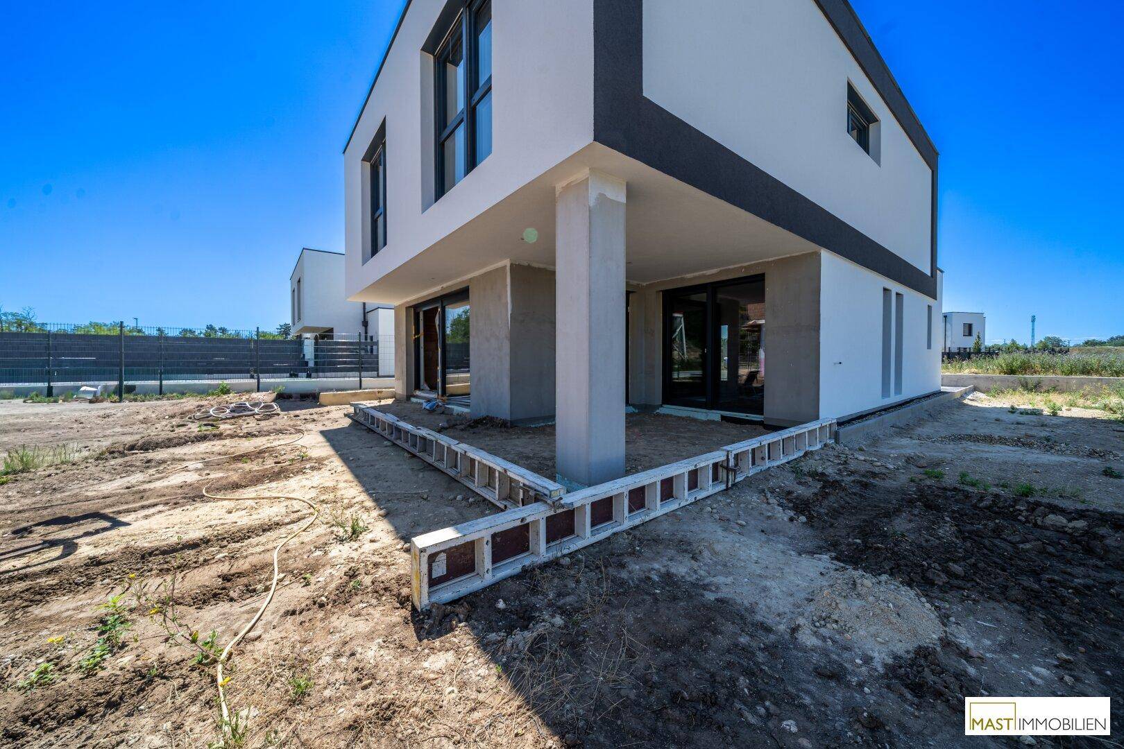 Überdachter Terrassenbereich im Rohbau an der Rückseite der modernen Doppelhaushälfte.