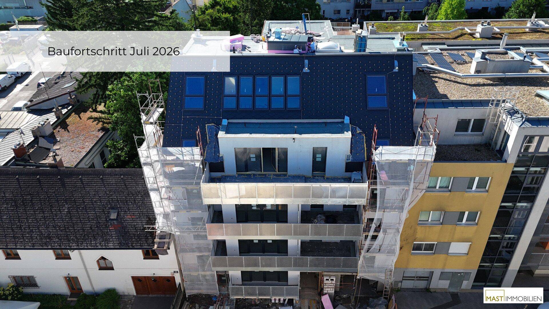 Draufsicht auf einen Neubau mit Gerüst, blauen Fenstern und Flachdach in der Bauphase.