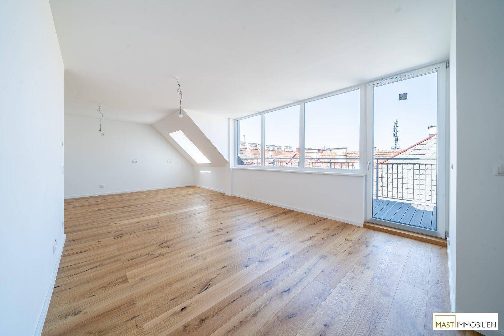 Heller offener Raum mit Holzboden, Balkonzugang und einem Dachfenster, bietet viel Gestaltungspotenzial.
