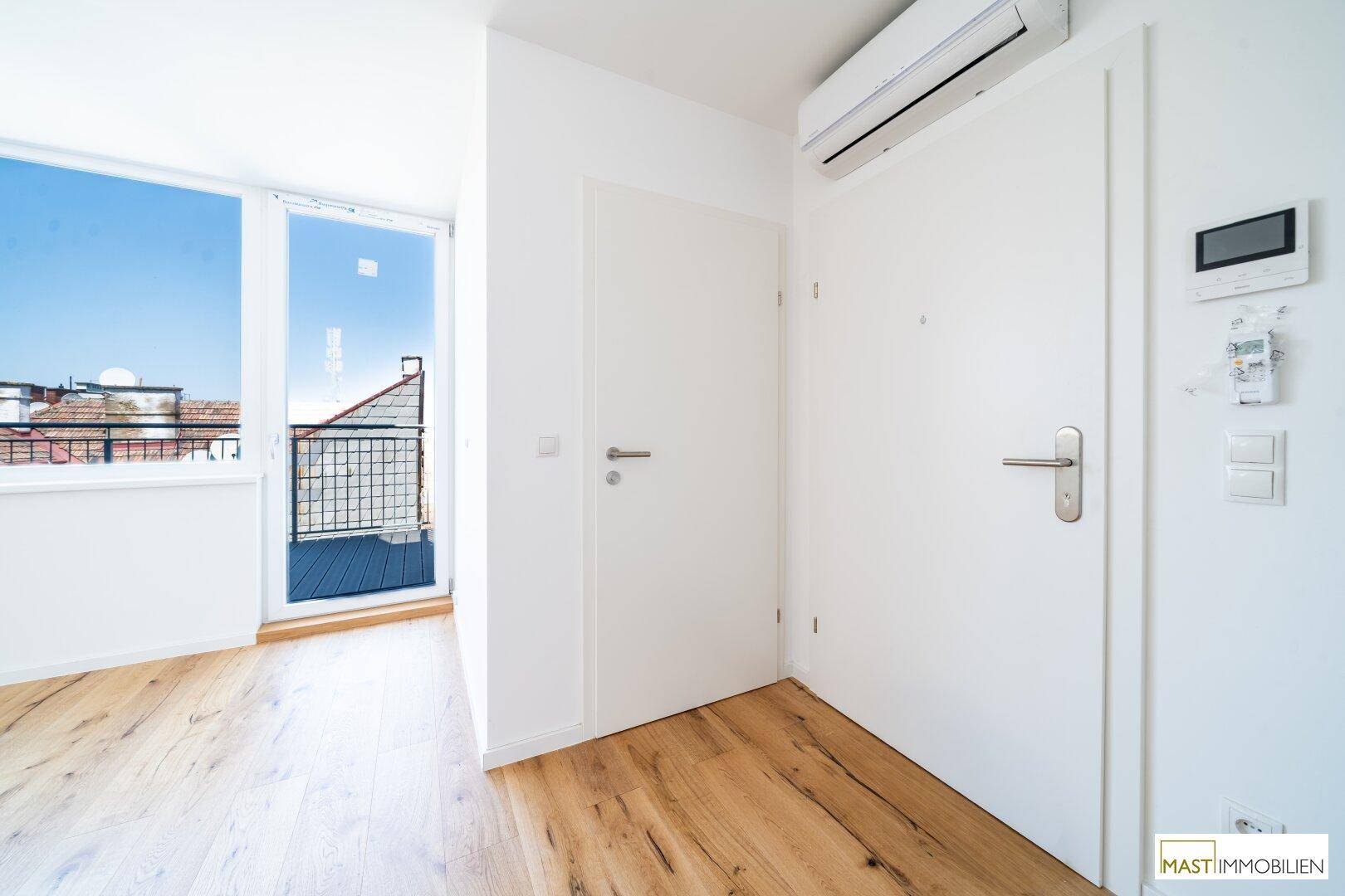 Heller Eingangsbereich mit Holzboden, Klimaanlage und Zugang zu einem Balkon, einladend und praktisch.