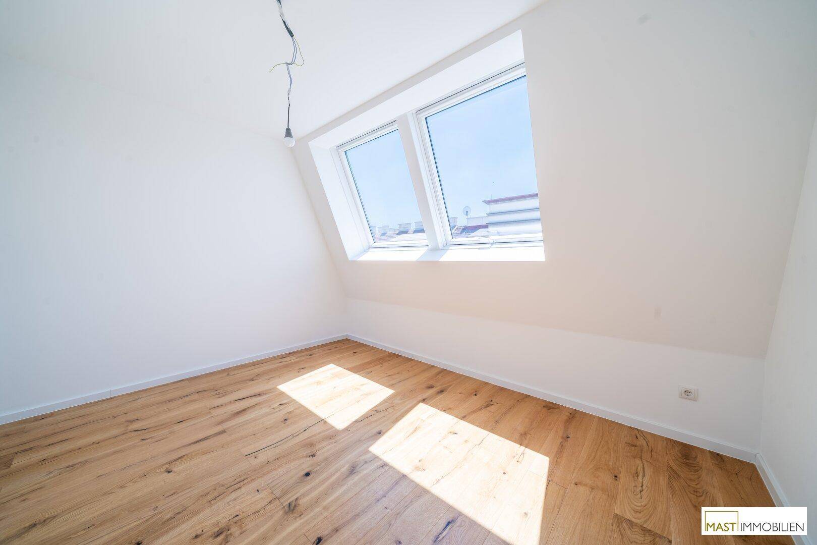 Helles Zimmer mit Holzboden und einem Dachfenster, vielseitig nutzbar als Kinder- oder Gästezimmer.
