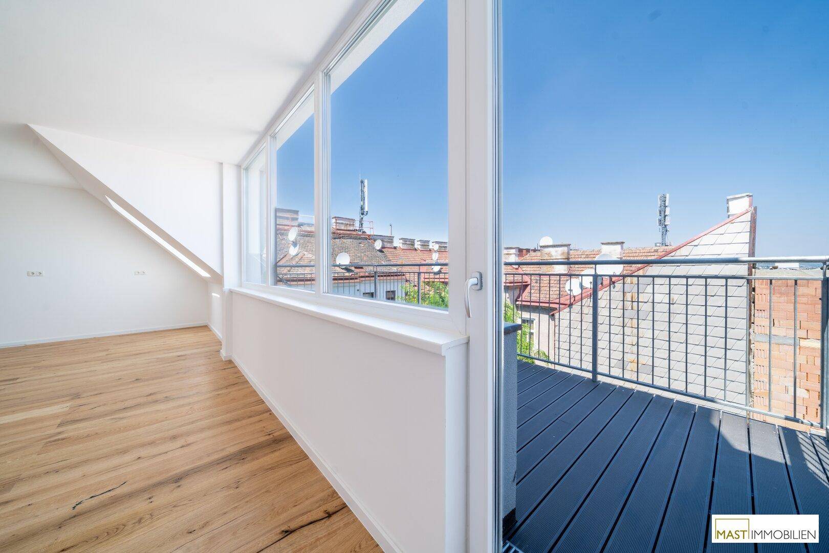 Geräumiger Balkon mit Holzdielen und Blick über die Dächer der Stadt, ideal zum Entspannen.