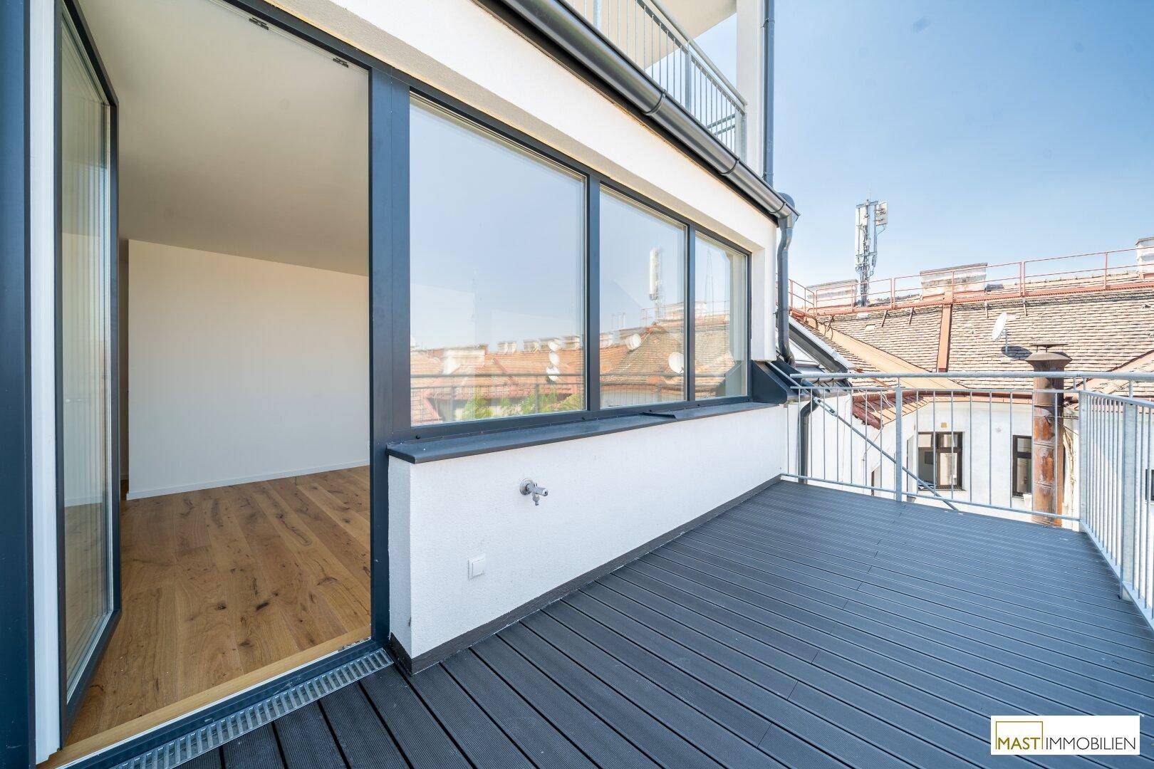Großer Balkon mit Holzdielen und Blick auf die umliegenden Gebäude, bietet viel Platz im Freien.