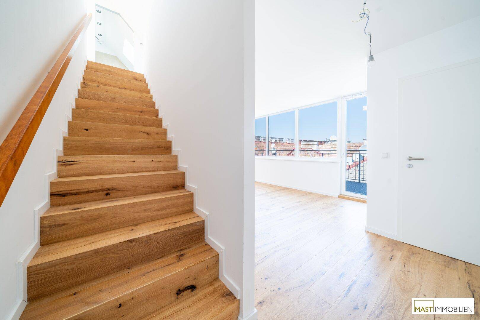 Elegante Holztreppe führt in die obere Etage, mit hellem Raum im Hintergrund, modern und stilvoll.