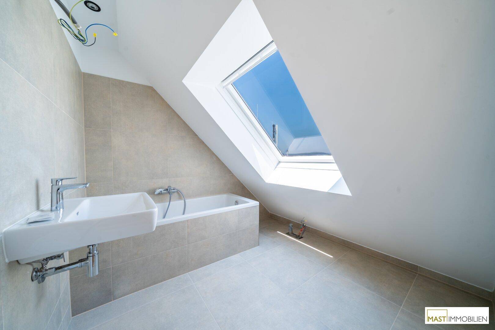 Helles Badezimmer im Dachgeschoss mit Badewanne, Waschbecken und großem Dachfenster.