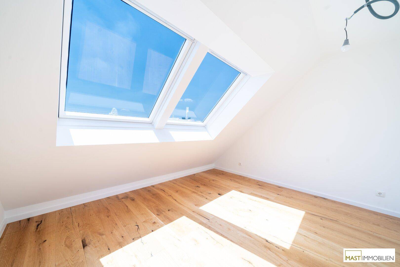 Heller Dachgeschossraum mit Holzboden und zwei großen Dachfenstern, ideal für individuelle Gestaltung.