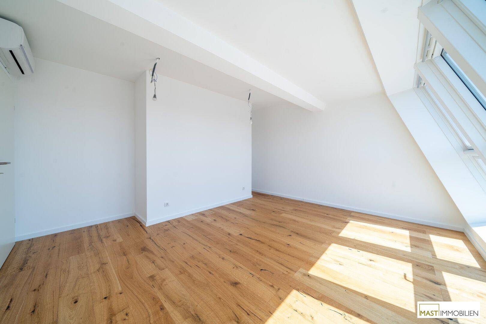 Lichtdurchfluteter Dachgeschossraum mit Holzboden, Klimaanlage und großem Dachfenster.