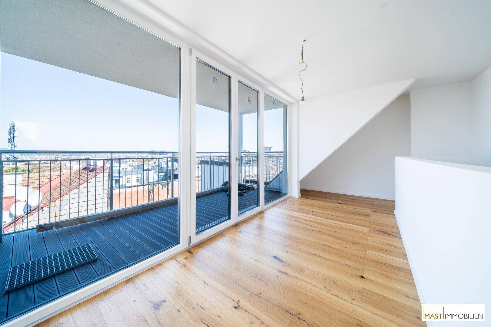 Heller Wohnbereich mit Holzboden, großen Glasfronten und Zugang zum Balkon, bietet viel Tageslicht.