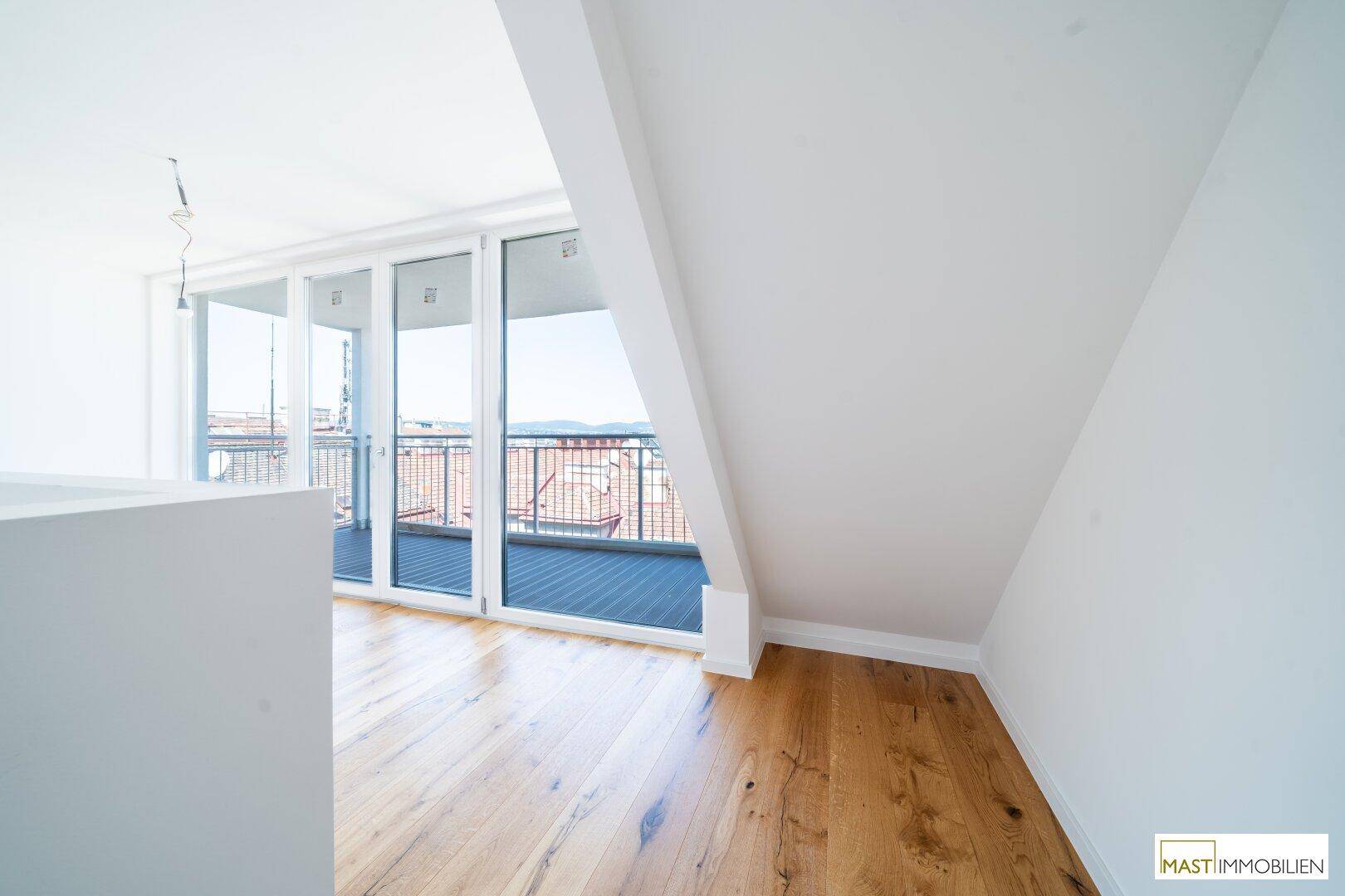 Heller Raum mit Holzboden und großen Fenstern, die Zugang zu einem Balkon mit Stadtblick bieten.