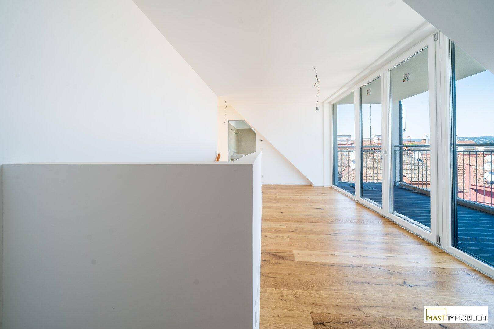 Lichtdurchfluteter Raum mit Holzboden und breiter Fensterfront, die einen weiten Blick ermöglicht.