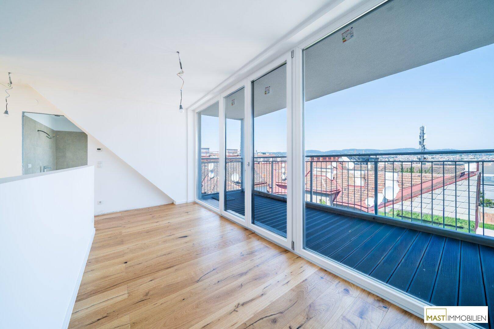 Geräumiger Raum mit Holzboden und Panoramafenstern, die einen direkten Zugang zum Balkon bieten.