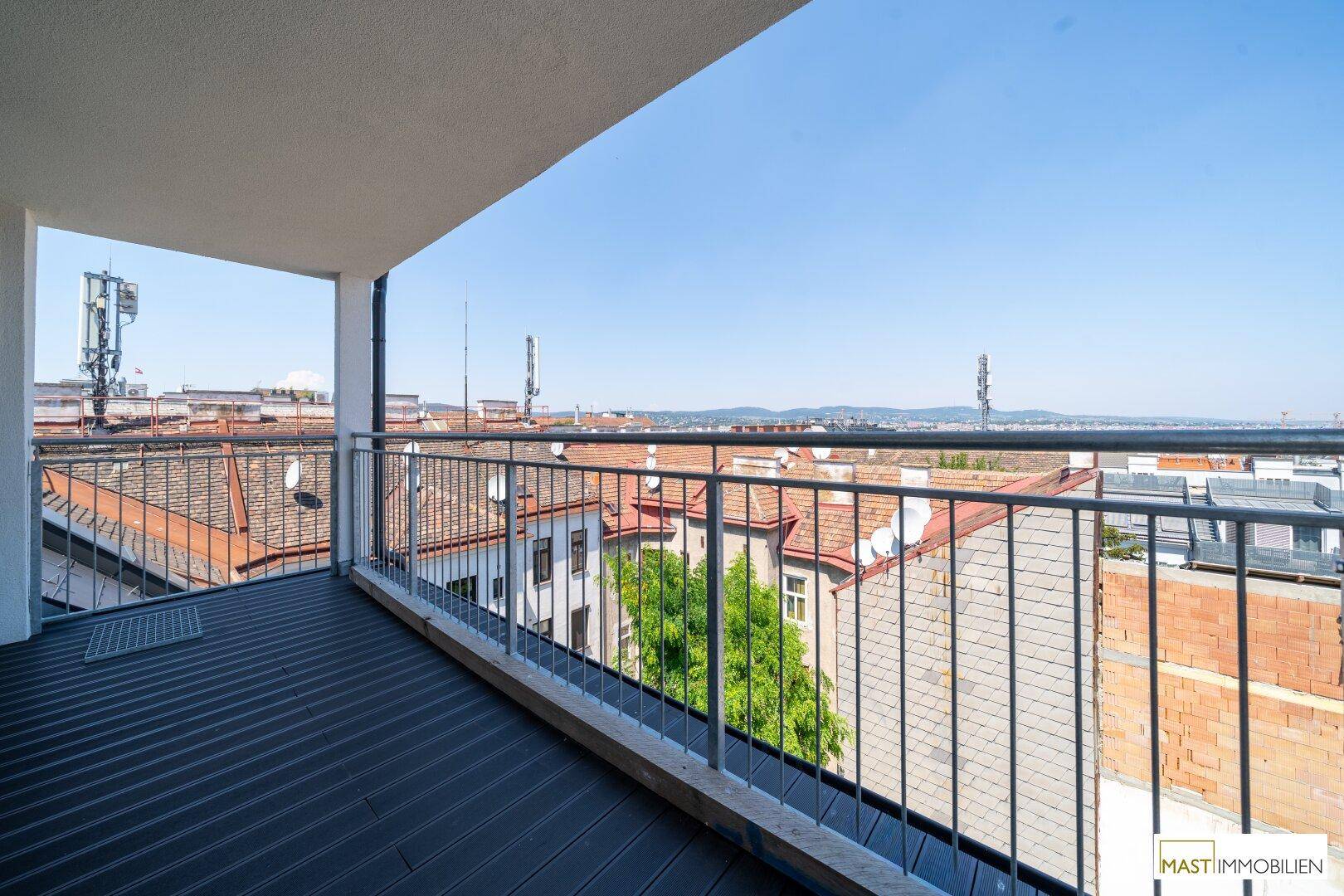 Geräumiger Balkon mit Holzdielen und weitem Blick über die Dächer der Stadt.