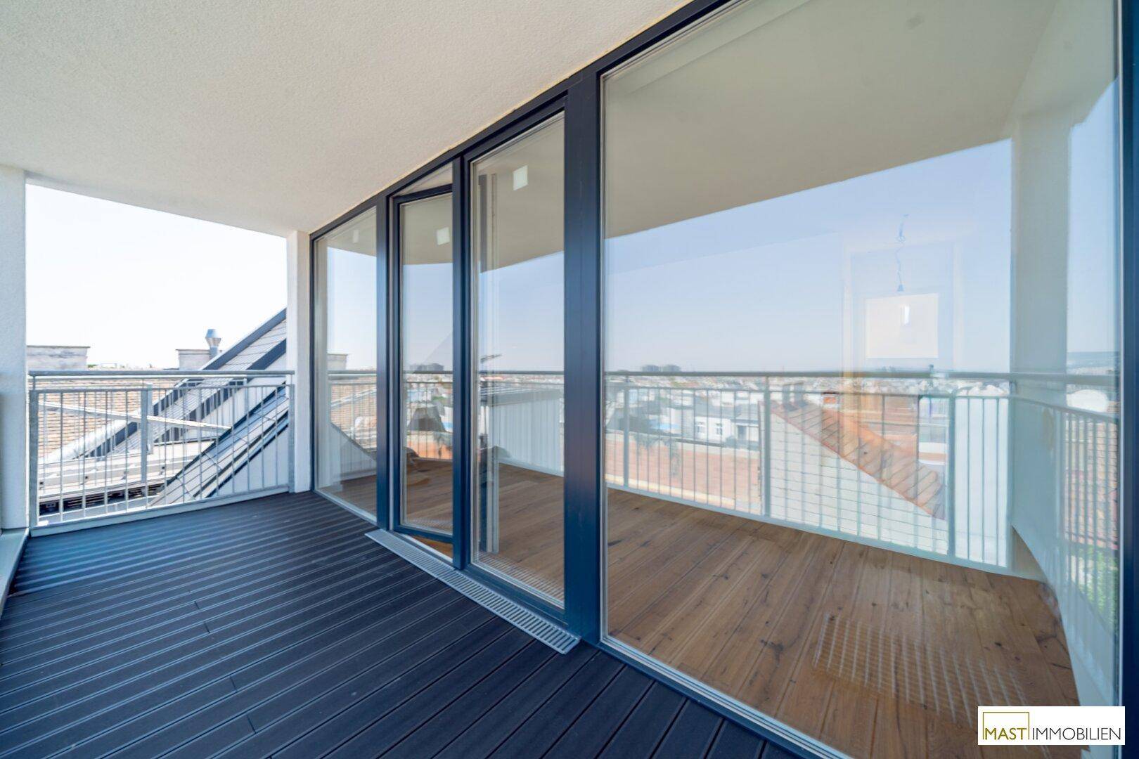 Moderner Balkon mit dunklem Bodenbelag und großen Glasschiebetüren zum Innenbereich.