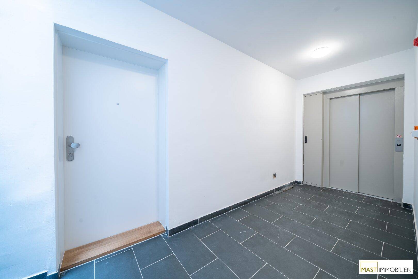 Eingangsbereich mit modernem Aufzug und dunklem Fliesenboden, hell und einladend.