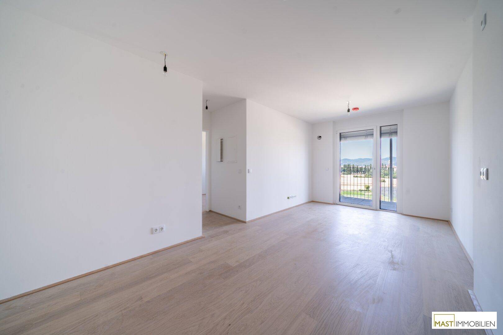 Heller, unmöblierter Wohnbereich mit Holzboden und Zugang zum Balkon.