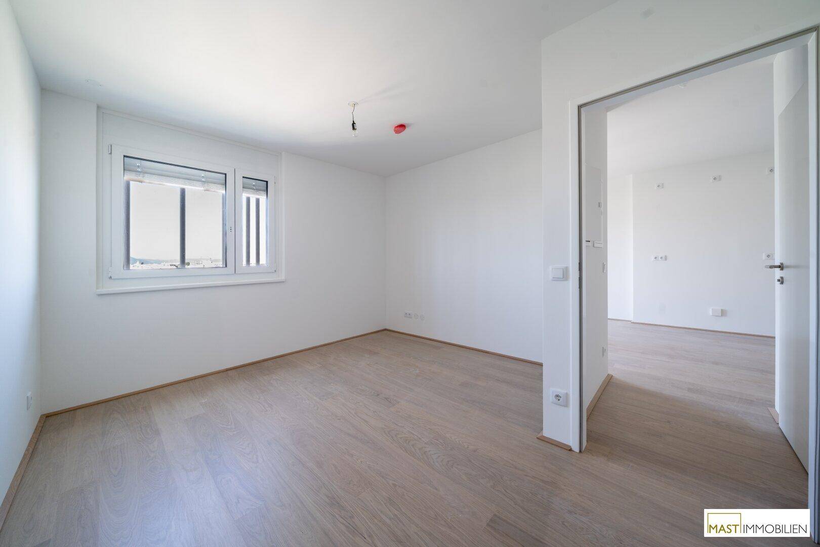 Helles Schlafzimmer mit Holzboden und großem Fenster, bereit zur Einrichtung.