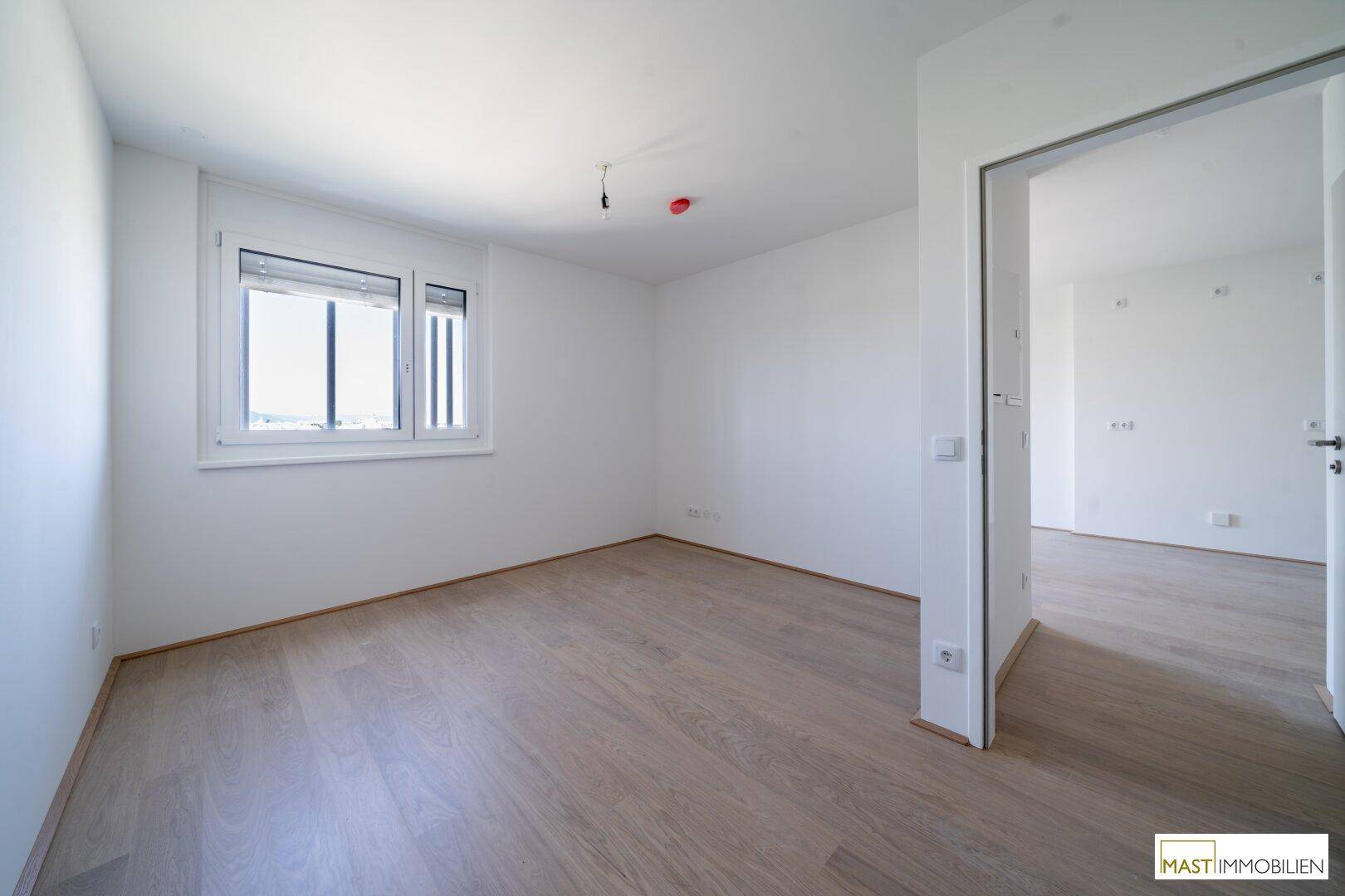 Geräumiges Schlafzimmer mit hellem Holzboden und viel Tageslicht.