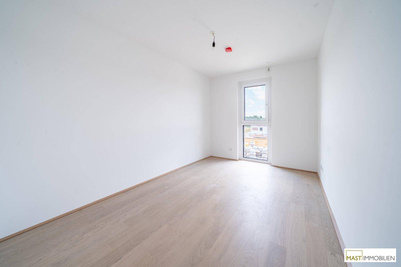 Helles Schlafzimmer mit Holzboden und einem Fenster, das einen Blick nach draußen bietet.