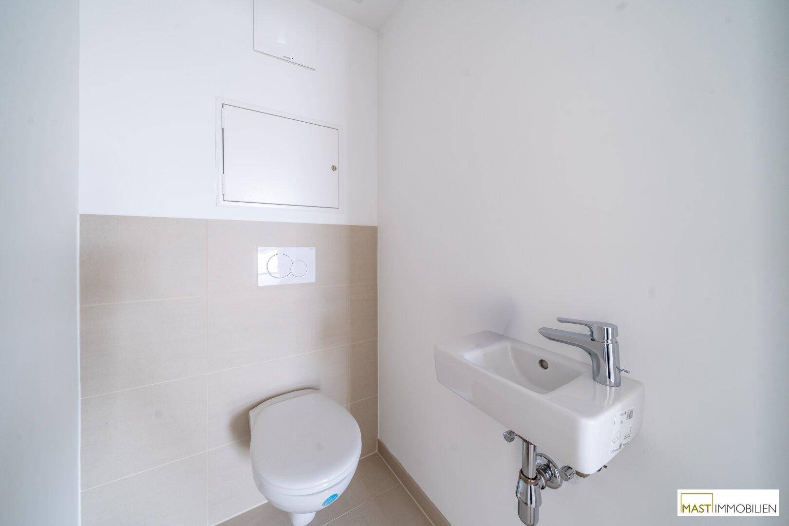 Modernes Gäste-WC mit Wand-WC und kleinem Waschbecken, hell gefliest.