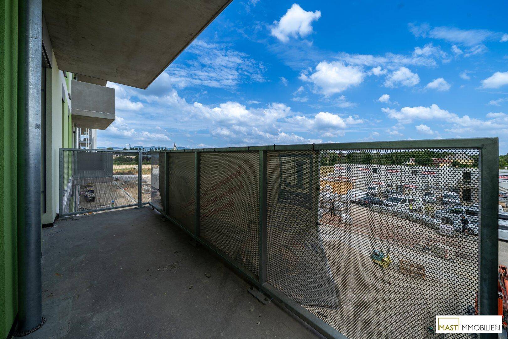 Geräumiger Balkon mit Metallgeländer und weitem Blick über die angrenzende Baustelle.