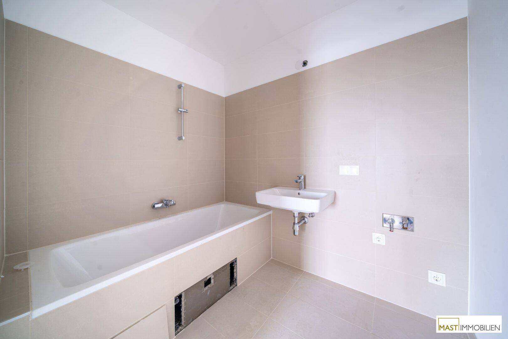 Geräumiges Badezimmer mit Badewanne und Waschbecken, bereit für den letzten Ausbau.