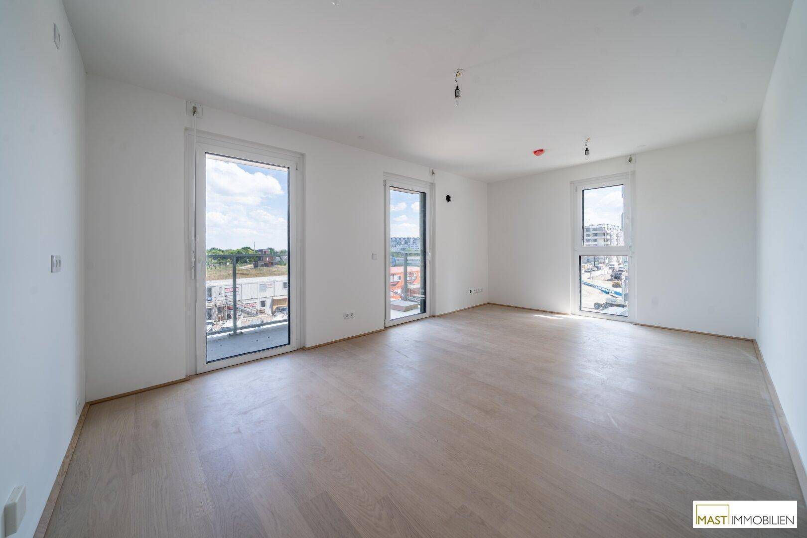 Geräumiges, helles Wohnzimmer mit großen Fenstern und Zugang zu einem Außenbereich.