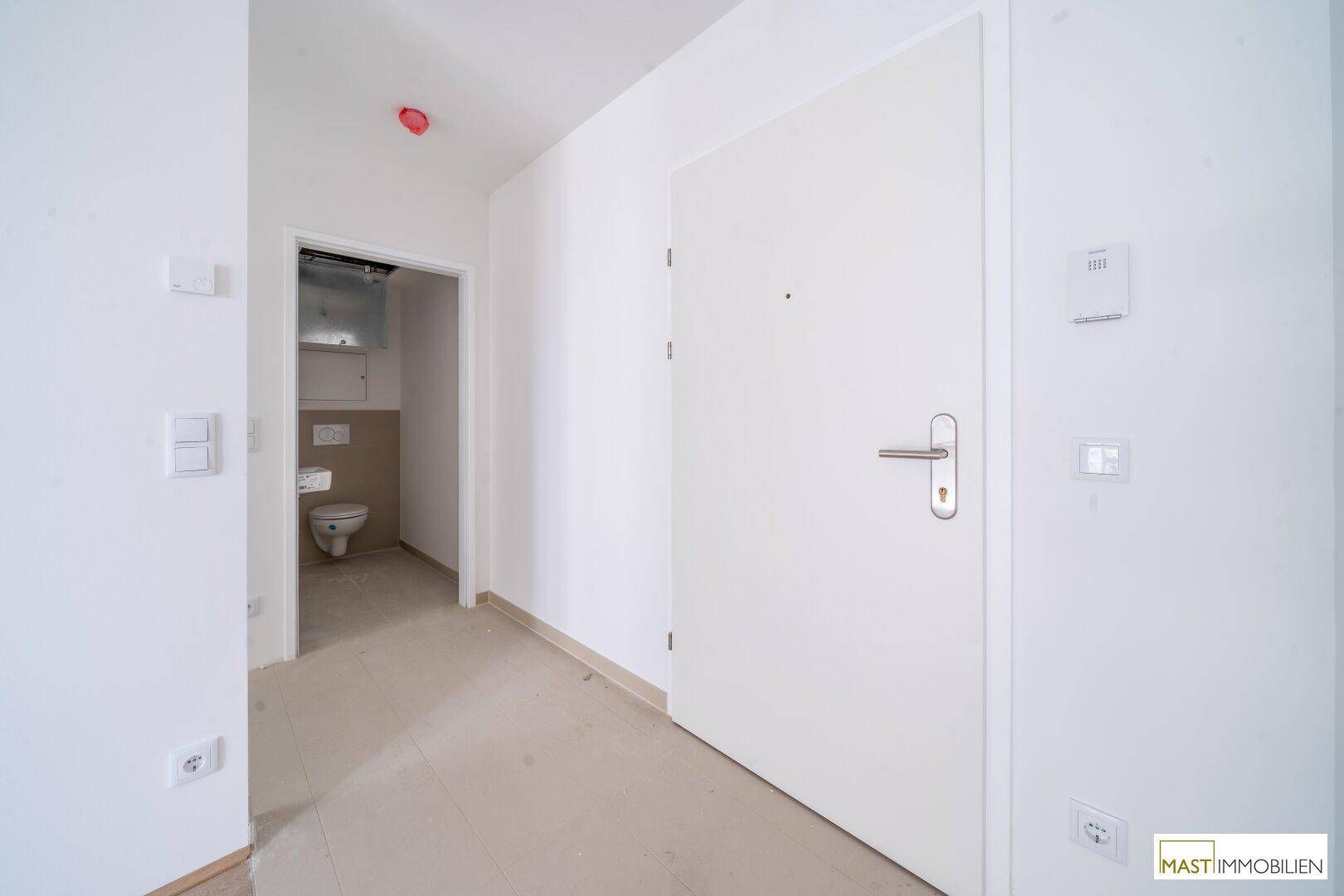 Eingangsbereich mit weißer Tür und Blick in ein separates Gäste-WC, hell und funktional.
