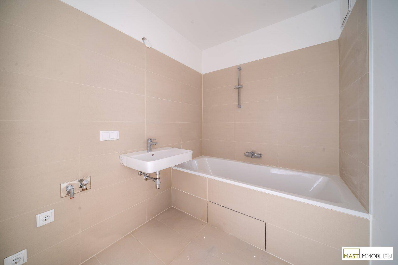 Modernes Badezimmer mit beigefarbenen Fliesen, integrierter Badewanne und einem einzelnen Waschbecken.