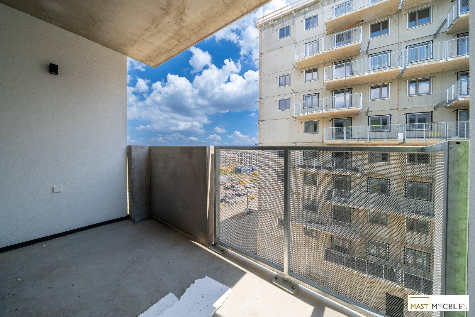 Geräumiger Balkon mit Betonboden und Metallgeländer, bietet Blick auf die umliegenden Gebäude.