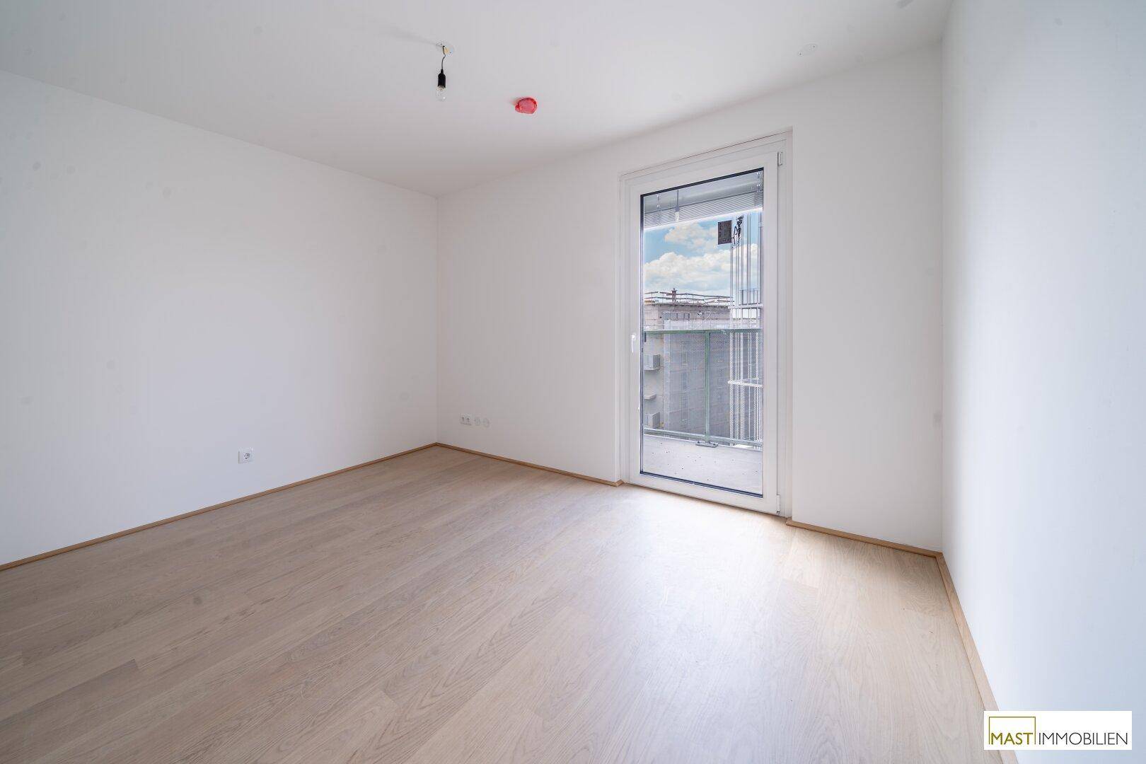 Helles Schlafzimmer mit neuem Holzfußboden und einem großen Fenster, das den Raum mit Licht füllt.