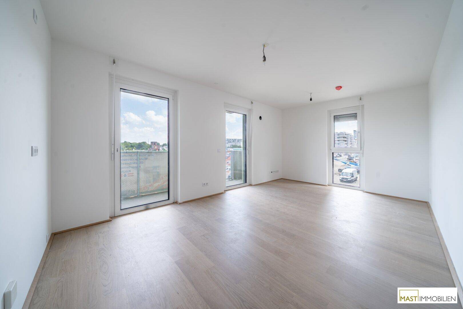 Helles, leeres Zimmer mit Holzboden und Zugang zu einem Balkon, bereit für die Einrichtung.