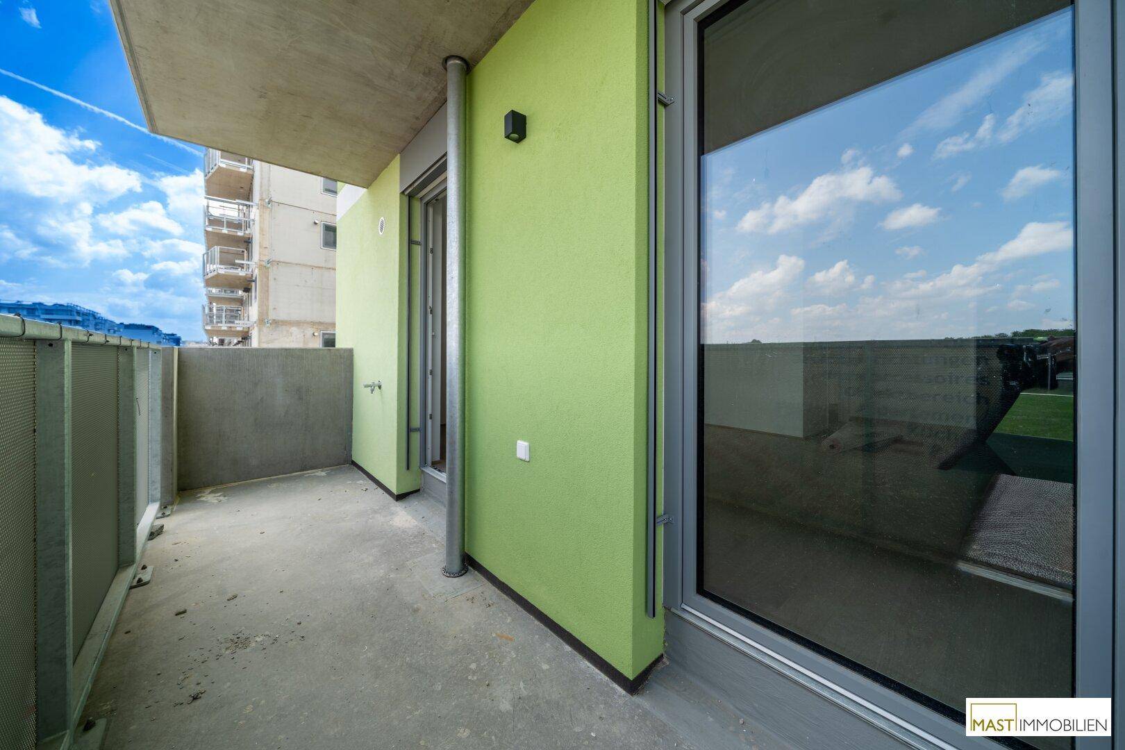 Geräumiger Balkon mit grüner Wand und Blick auf die Umgebung unter blauem Himmel.