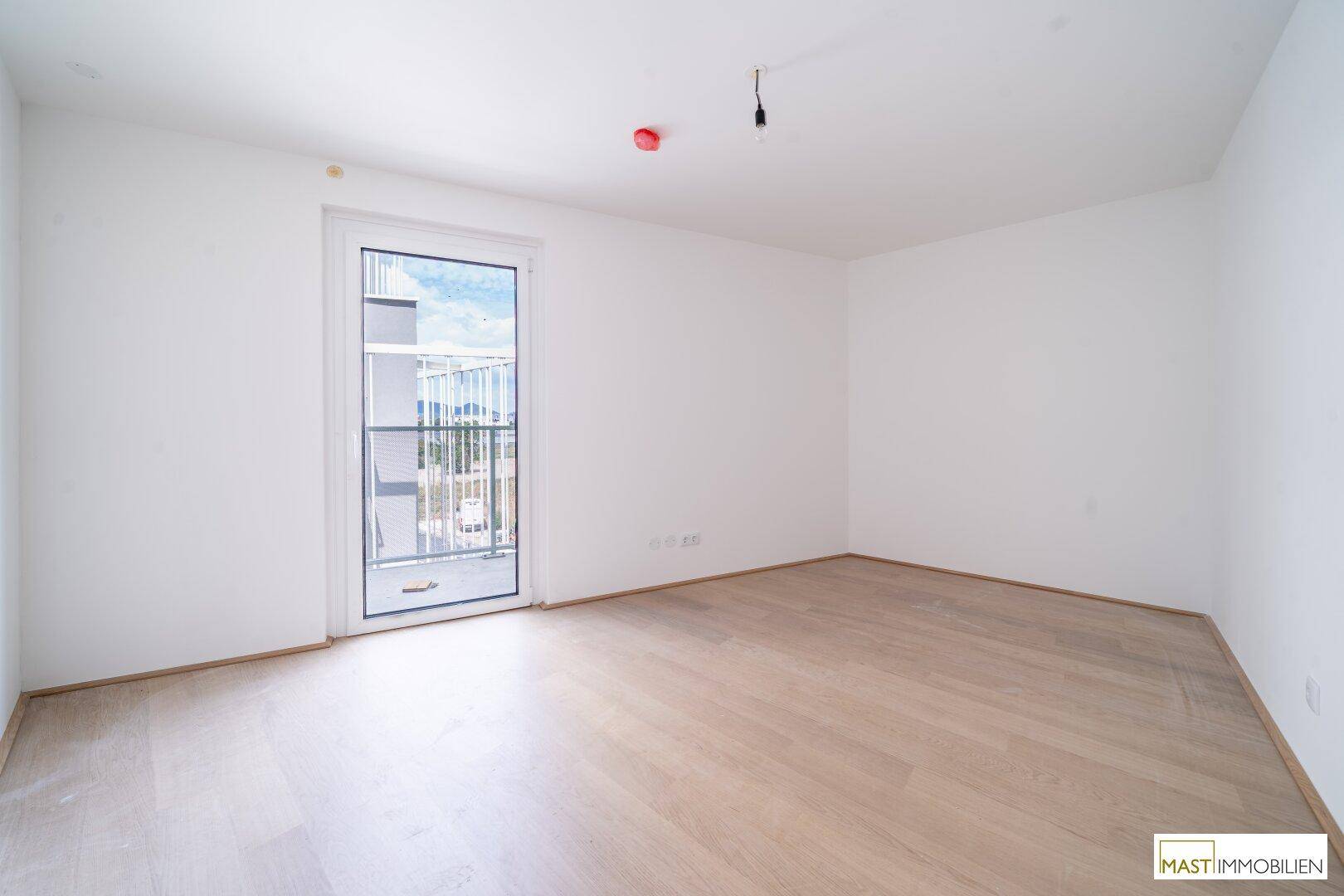 Helles Schlafzimmer mit Parkettboden und direktem Zugang zu einem Balkon.