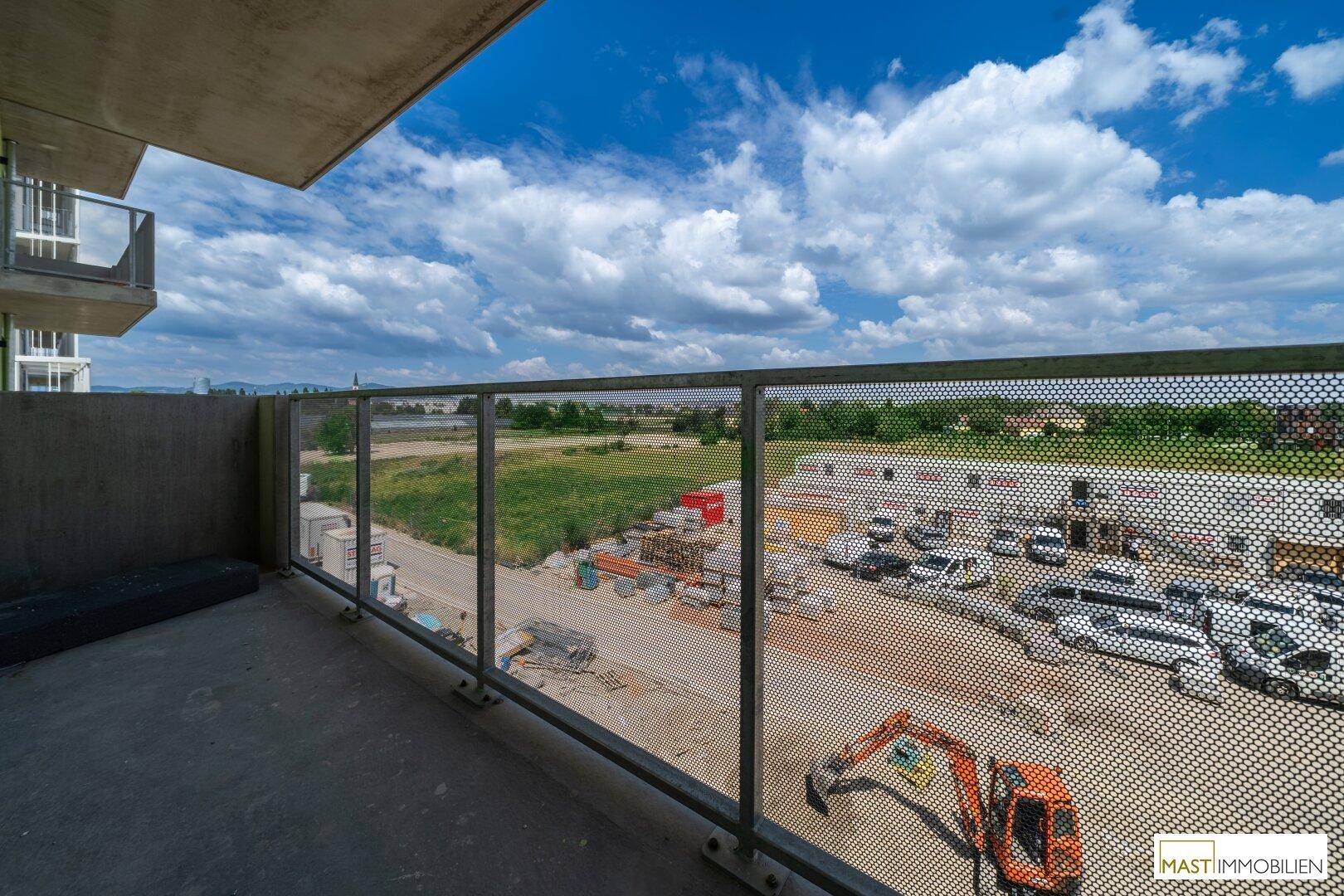 Geräumiger Balkon mit Metallgeländer und weitem Blick über die Baustelle und Landschaft.