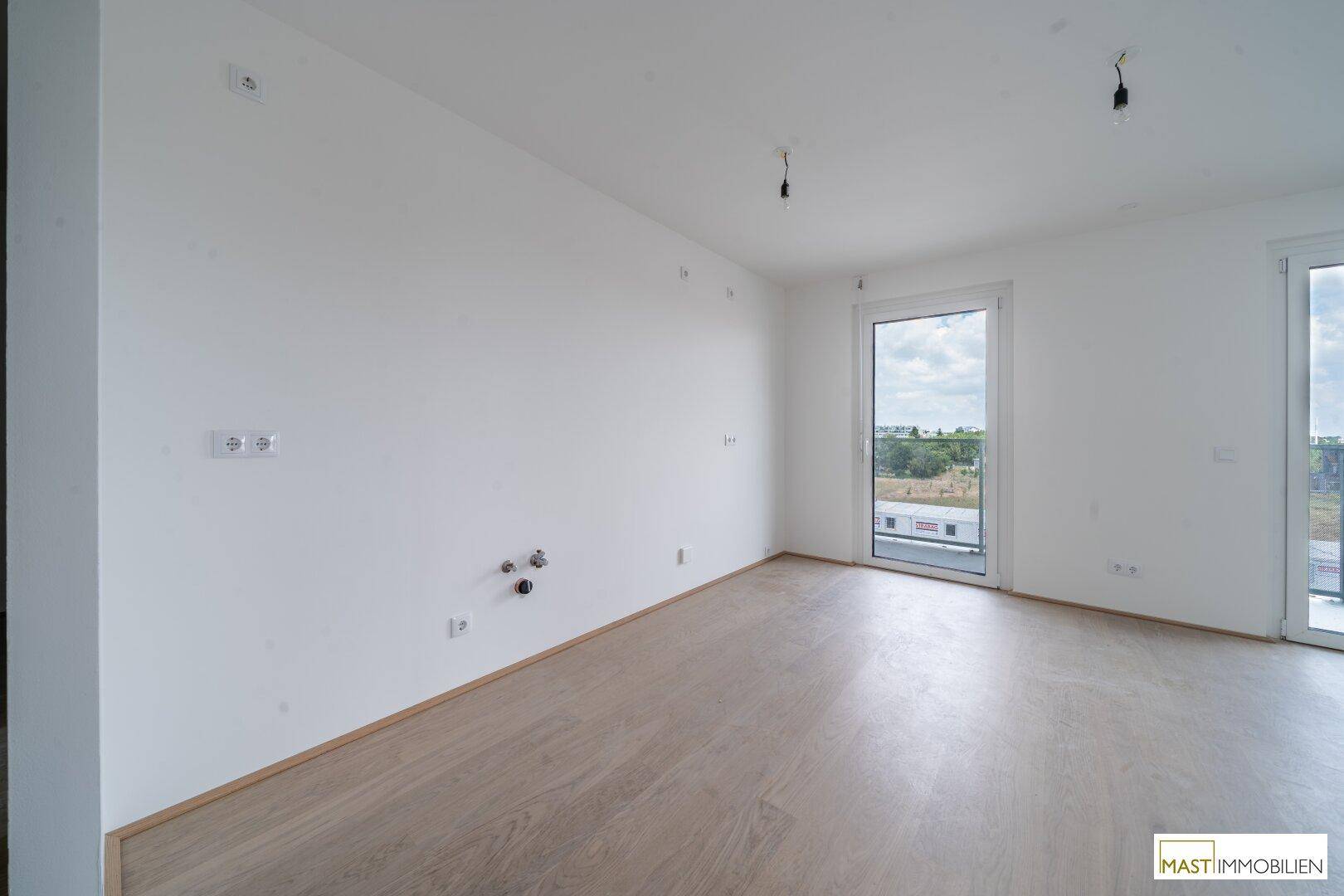 Leerer Küchenbereich mit Anschlüssen für eine moderne Einbauküche und direktem Balkonzugang.