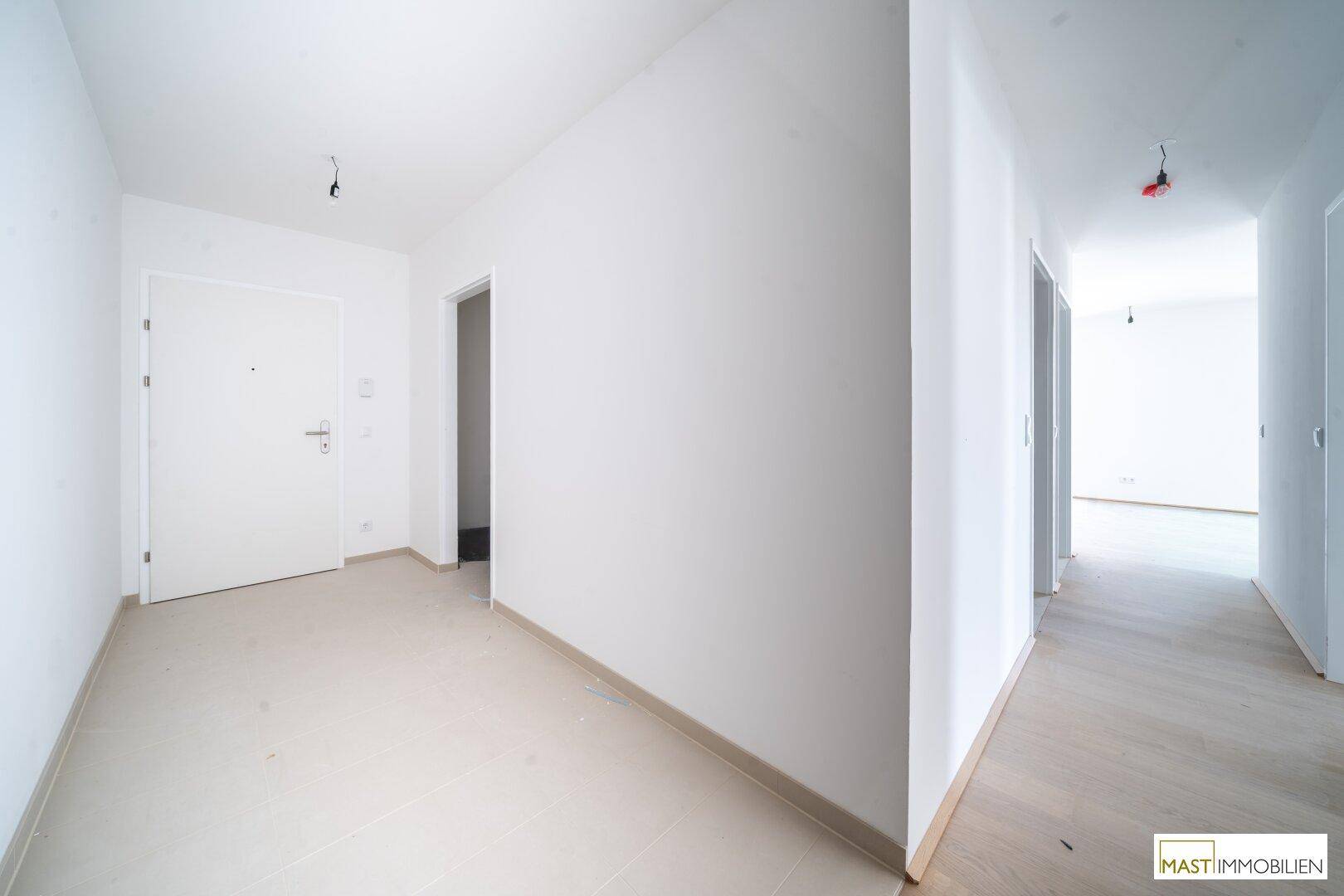 Eingangsbereich mit weißer Tür, Fliesenboden und Übergang zu einem Zimmer mit Holzboden.