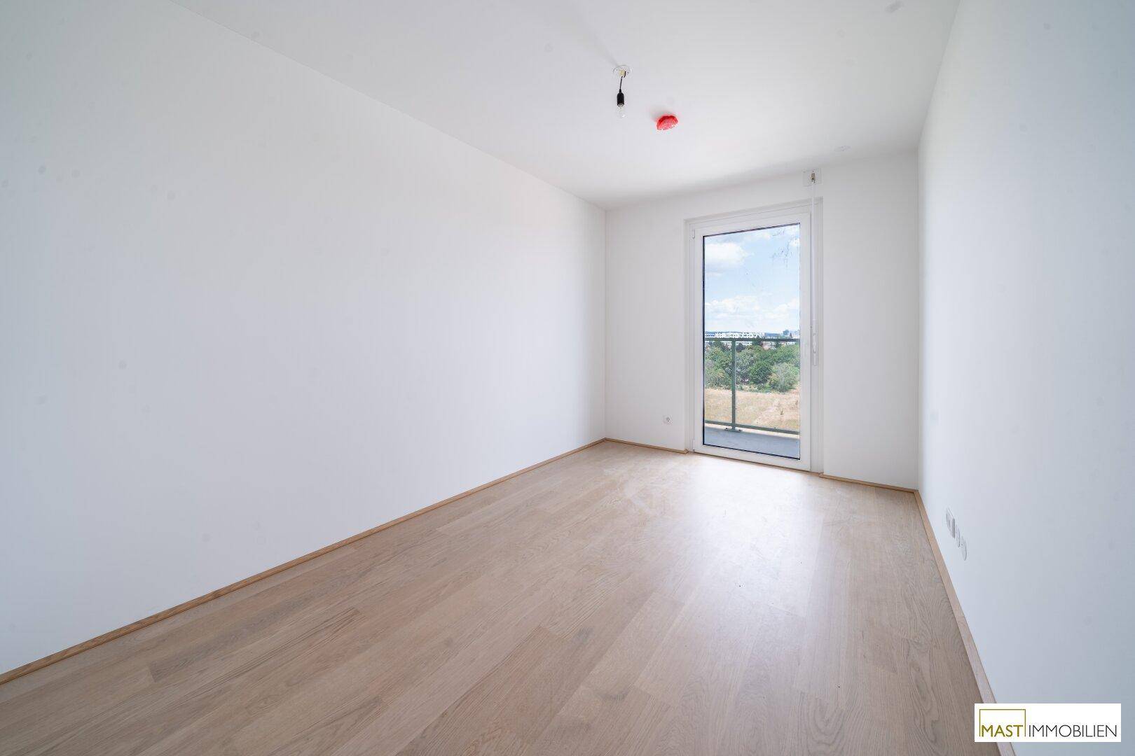 Unmöbliertes Zimmer mit hellem Holzboden und Zugang zu einem Balkon oder einer französischen Brüstung.