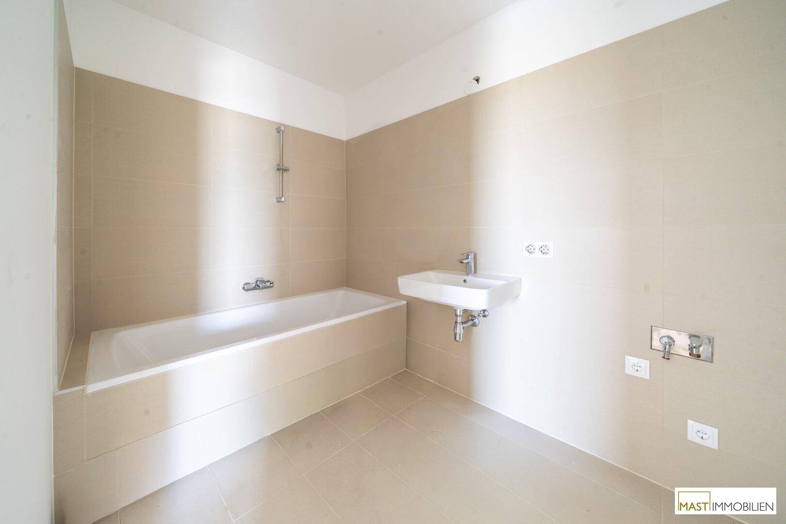 Modernes Badezimmer mit Badewanne, Einzelwaschbecken und beigefarbenen Fliesen an Wänden und Boden.