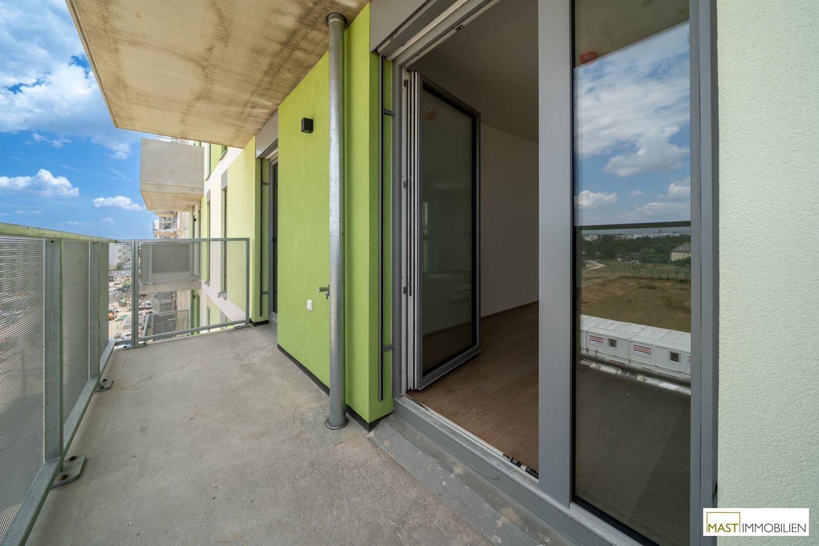 Geräumiger Balkon mit Betonboden, Metallgeländer und Blick auf die Umgebung.