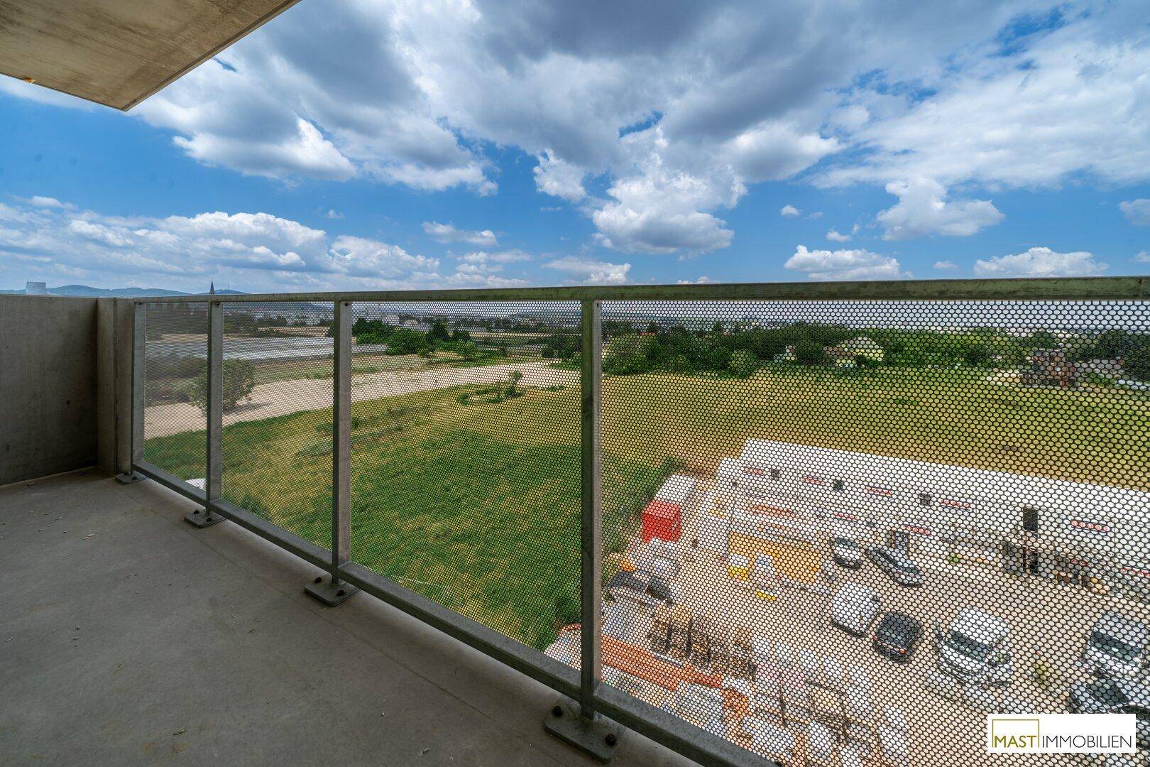 Weitläufiger Ausblick vom Balkon über eine Baustelle und grüne Landschaft.