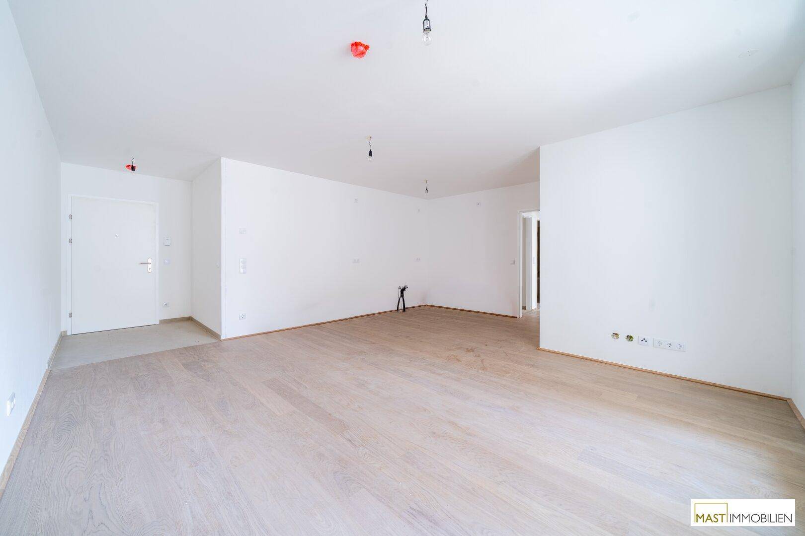 Geräumiges, unmöbliertes Wohnzimmer mit Holzboden und weiß gestrichenen Wänden.
