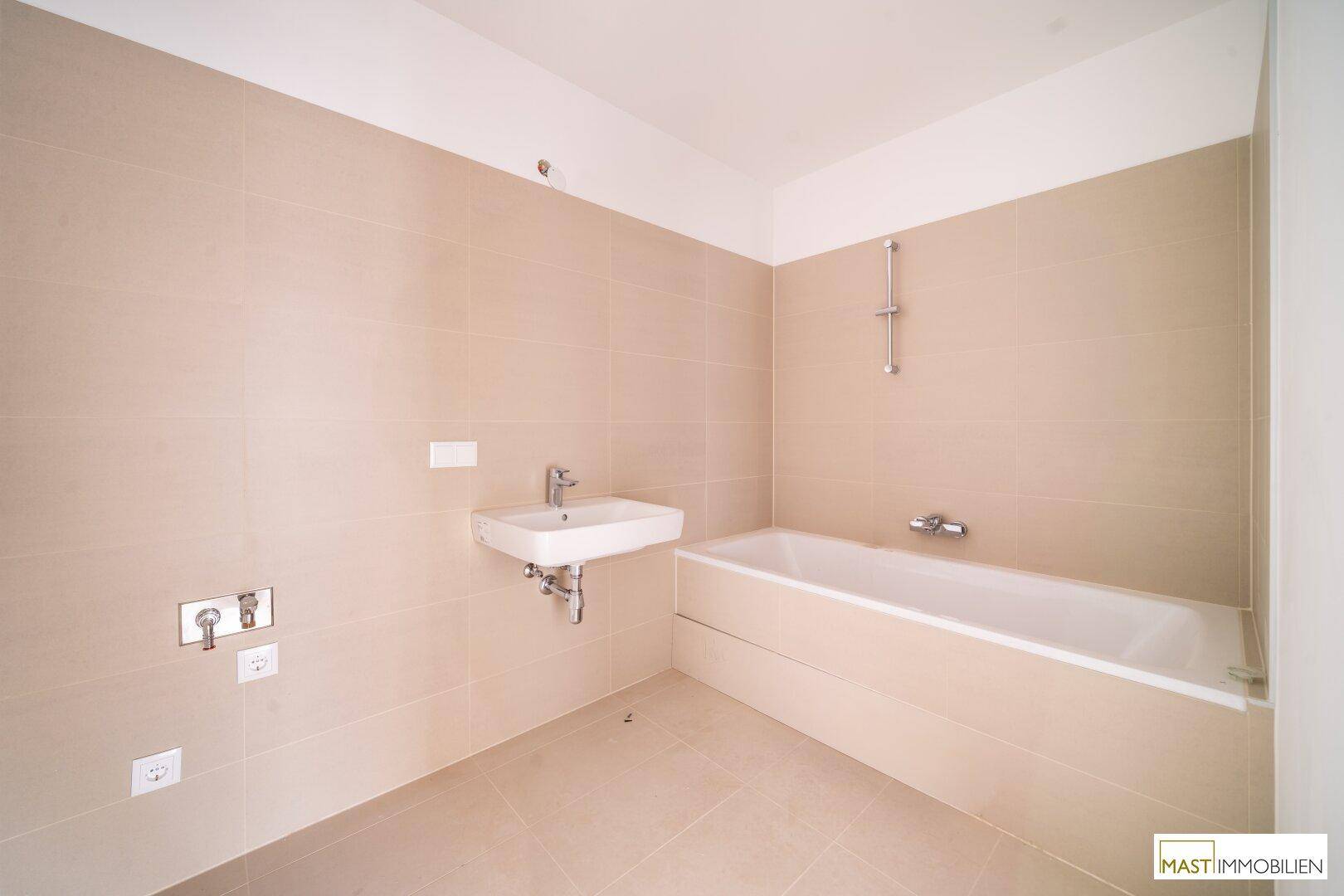 Modernes Badezimmer mit Badewanne, Waschbecken und beigefarbenen Fliesen.