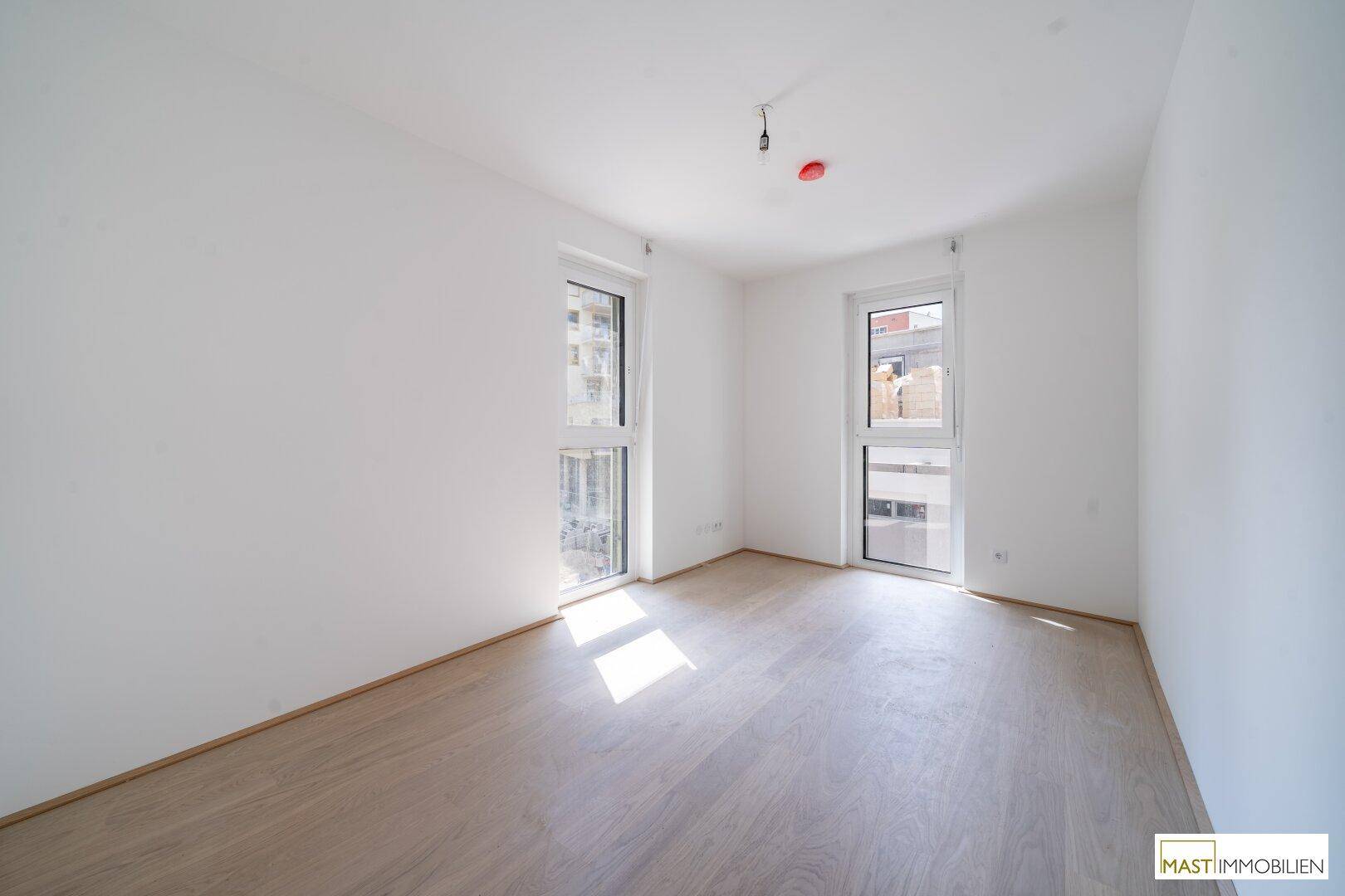 Helles, unmöbliertes Zimmer mit zwei Fenstern und Holzboden, ideal als Schlafzimmer.