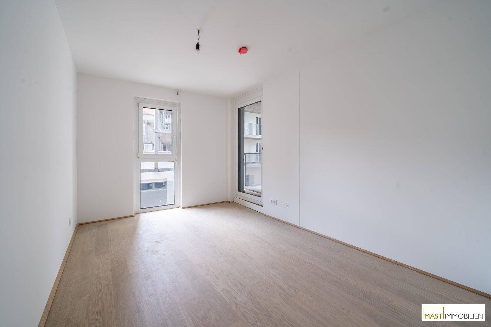 Leeres Schlafzimmer mit großen Fenstern, die viel Tageslicht hereinlassen.