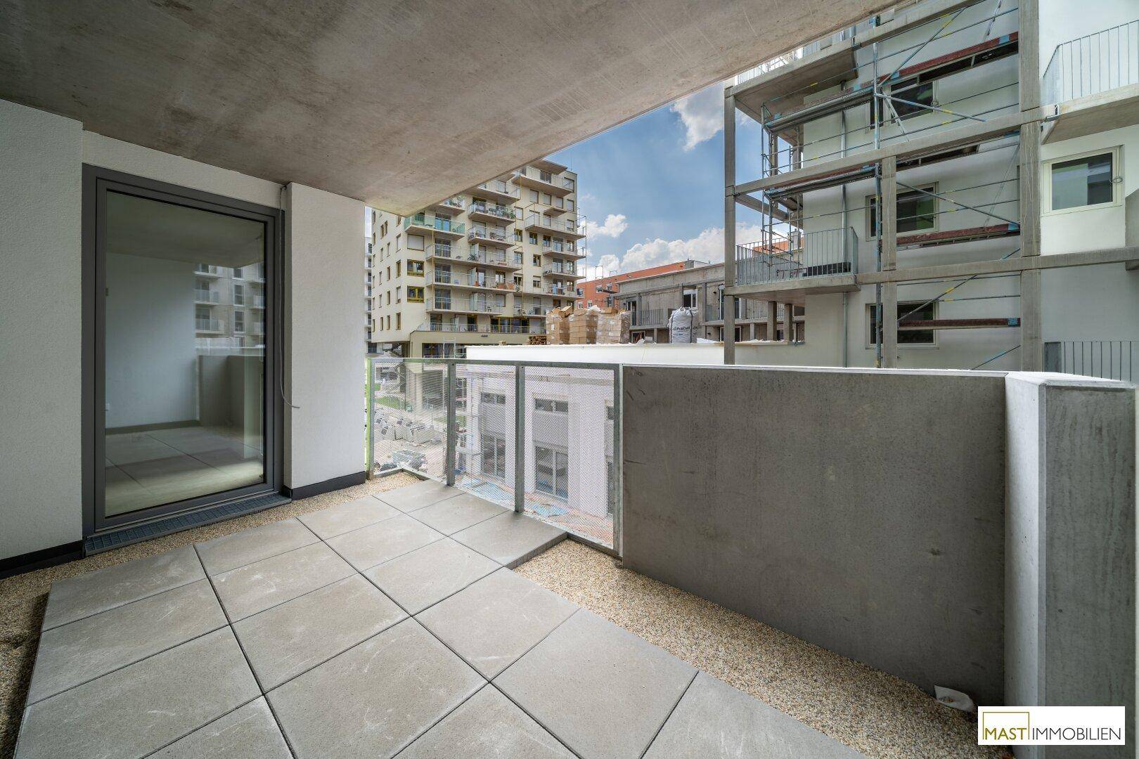 Großer Balkon mit Fliesen und Blick auf die Baustelle und Nachbargebäude.